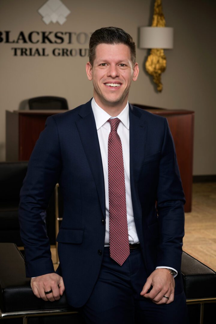 A man in a navy suit and red tie smiling indoors.