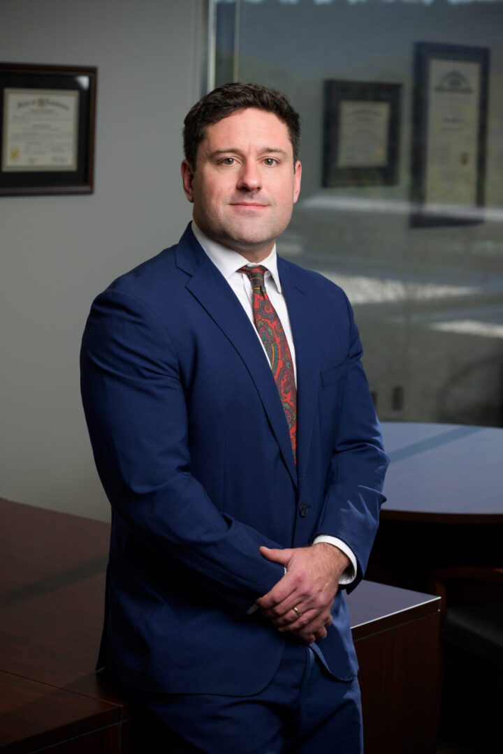 Professional man in a navy suit posing in an office setting.