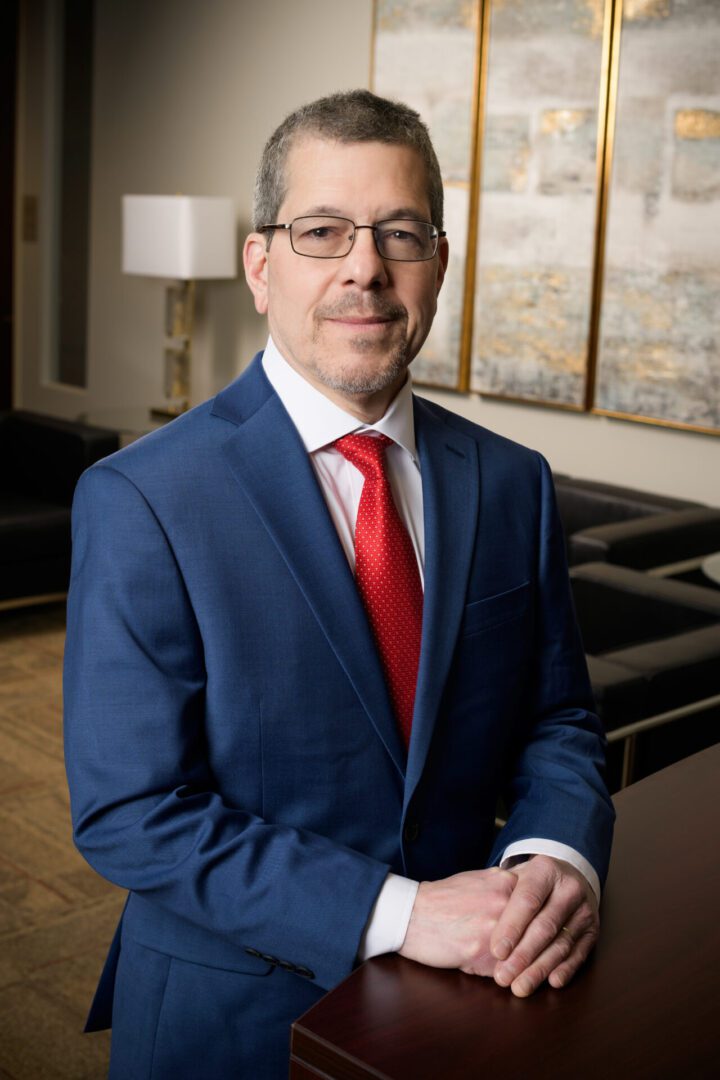 Professional man in blue suit and red tie standing indoors.