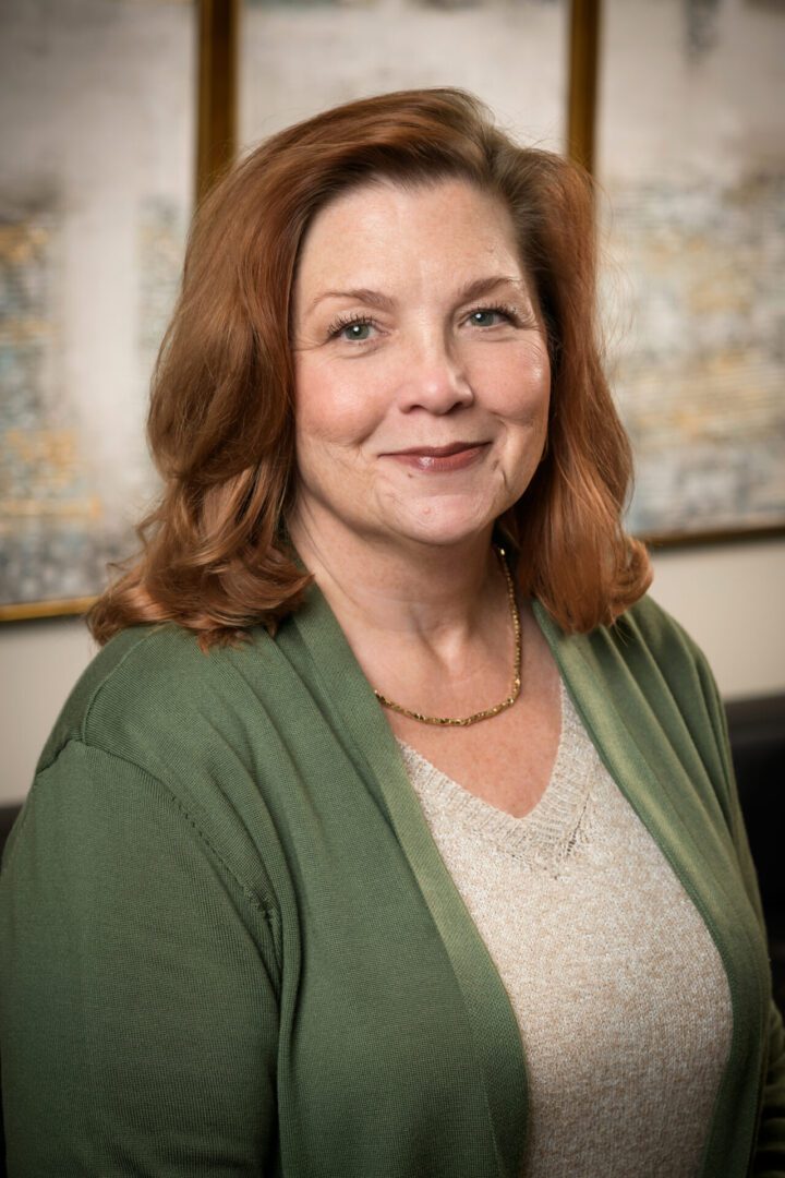 Professional portrait of a woman with red hair wearing a green cardigan.