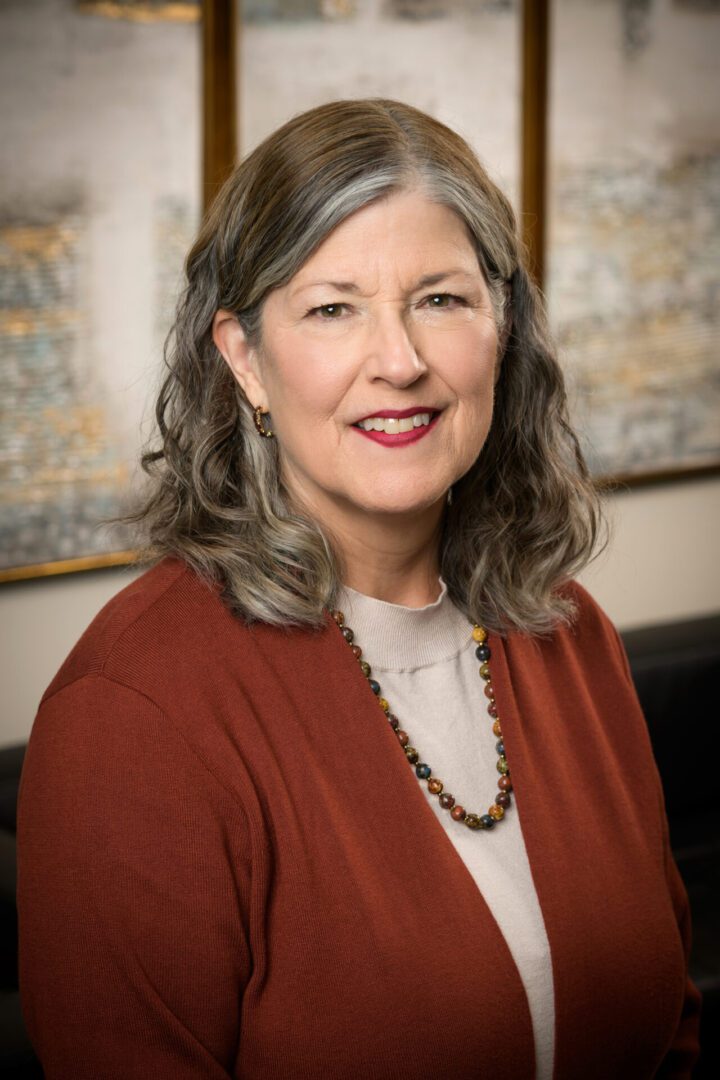 Portrait of a smiling woman wearing a rust-colored cardigan and necklace.