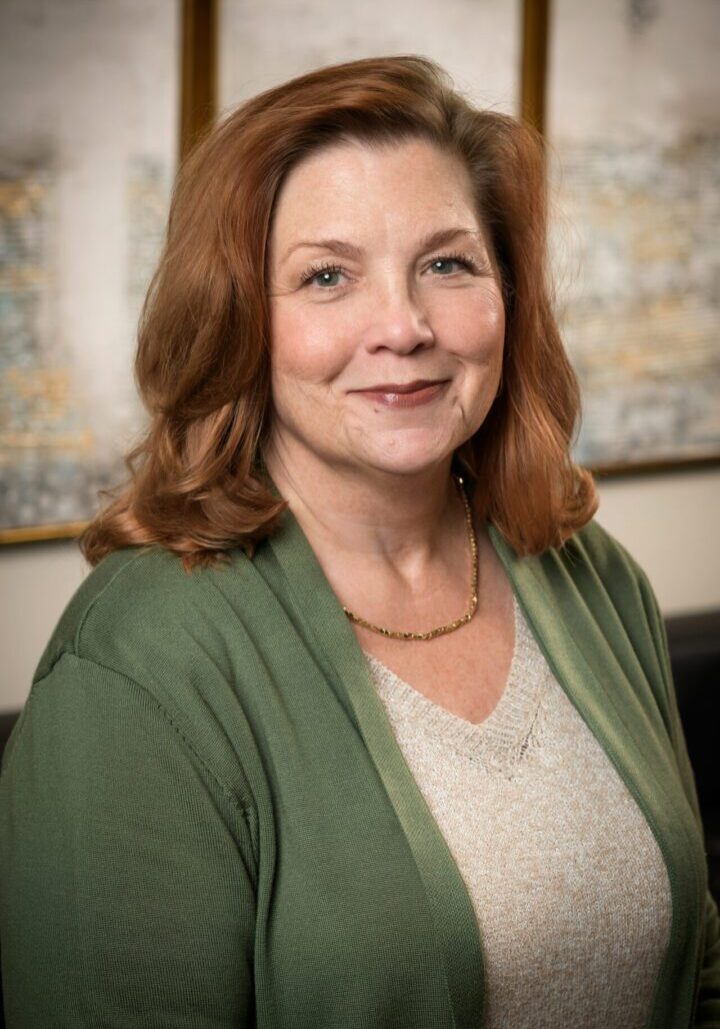 Professional portrait of a woman with red hair wearing a green cardigan.